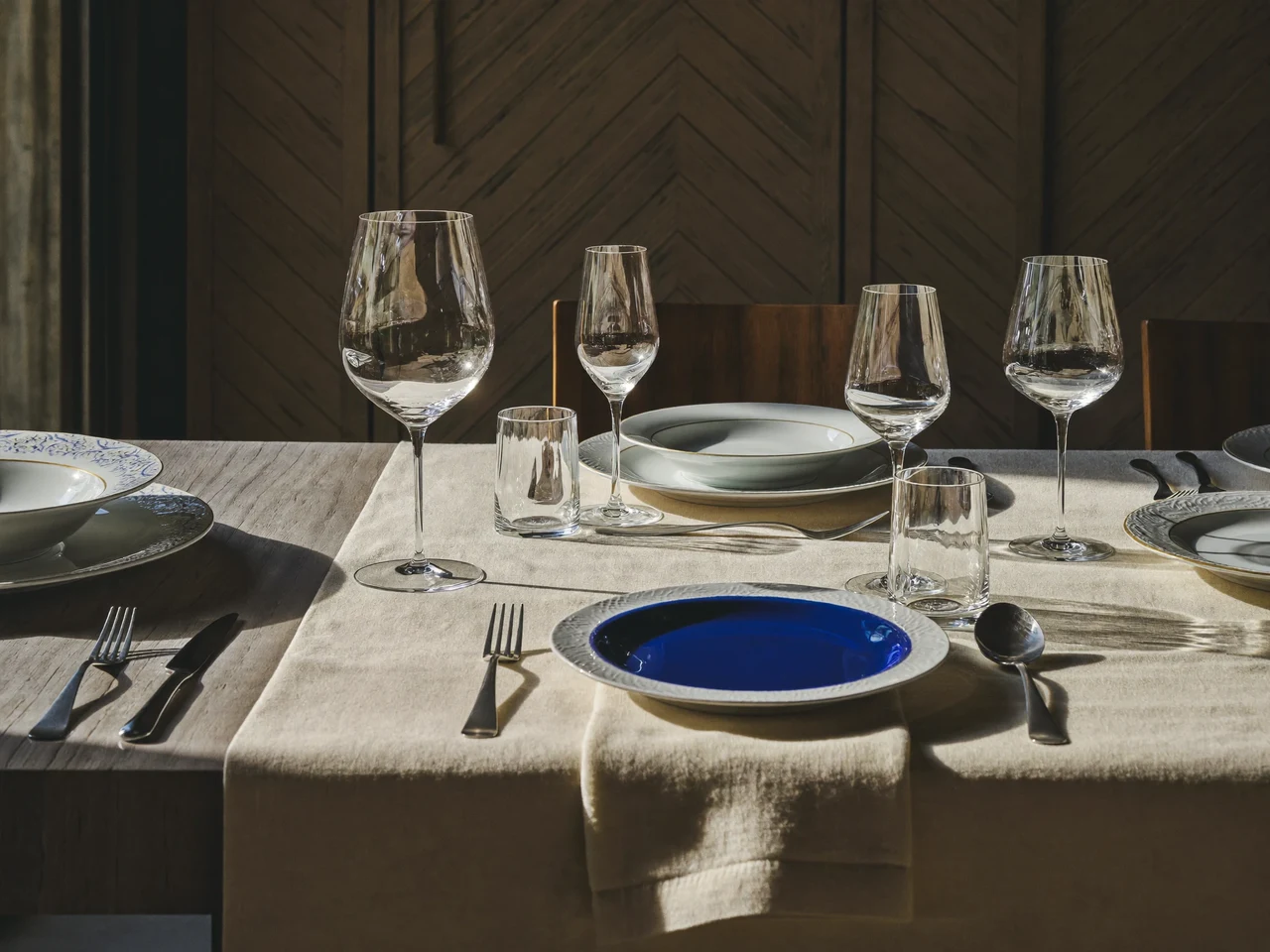 Gedeckter Tisch mit Tellern, Gläsern, Besteck und kobaltblauen Keramikakzenten im Schaufensterstil