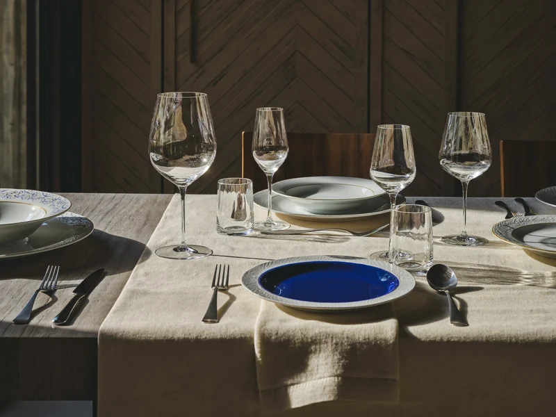 Gedeckter Tisch mit Tellern, Gläsern, Besteck und kobaltblauen Keramikakzenten im Schaufensterstil